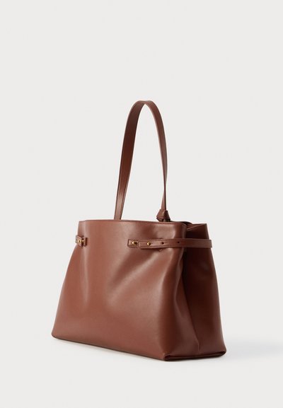 Καφέ δερμάτινη τσάντα tote με λεία υφή, μακριά χερούλια και διακριτικές χρυσαφένιες λεπτομέρειες. Διαθέτει μινιμαλιστικό σχεδιασμό και ορθογώνιο σχήμα.