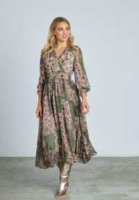 Abito lungo in stampa floreale e patchwork con sfumature di verde e malva. Maniche lunghe e vita stretta. Indossato con stivali argentati fino al ginocchio.