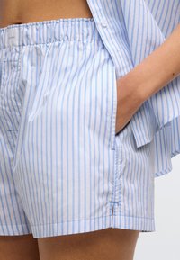 Ανοιχτά μπλε και λευκά ριγέ σορτς από μαλακό ύφασμα, με ελαστική μέση, πλαϊνές τσέπες και χαλαρή εφαρμογή.