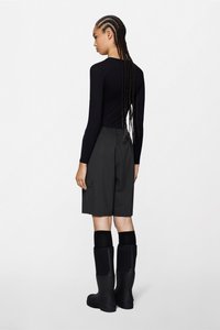 Μαύρο μακρυμάνικο τοπ, γκρι cargo σορτς με πλαϊνές τσέπες και μαύρες λαστιχένιες μπότες μέχρι το γόνατο. Τα μαλλιά είναι πλεγμένα σε μακριές κοτσίδες.