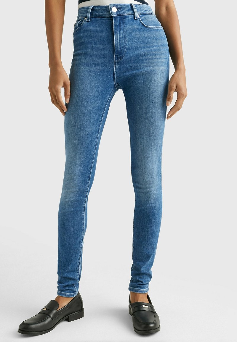 Kapej jeansit vaaleansinisestä denimistä, korkeavyötäröinen malli, jossa on viisi taskua ja kevyesti haalistuneita alueita. Mustat loafers-kengät yhdistettynä niihin.