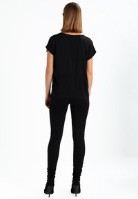 Top negro de manga corta con un corte relajado, combinado con jeans skinny negros y zapatos de tacón alto, visto desde la parte trasera.