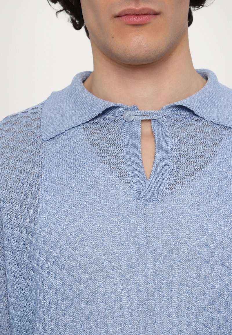 Maglione lavorato a maglia di colore azzurro con colletto e dettaglio a chiave. La texture è a maglia aperta con un motivo a nido d'ape e una piccola chiusura con bottone.