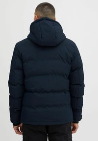 Chaqueta de plumas azul marino con capucha, que presenta secciones acolchadas, textura suave y puños elásticos. La vista posterior no muestra logos ni patrones visibles.