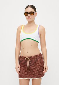 Bralette bianco strutturato con spalline multicolori; dettagli verdi, arancioni e viola. Gonna in crochet marrone con cordoncino e orlo a onde.