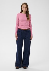 Rózsaszín hosszú ujjú póló bordázott mintázattal, sötétkék, bőszárú farmernadrággal és barna övvel párosítva. Egyszerű, letisztult dizájn.