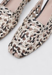 Zapatos planos tejidos que presentan tonos metálicos en oro, negro y crema. Diseño abierto con punta cuadrada y un acabado texturizado.