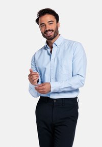 Lichtblauw button-up shirt met een zak; katoenmix stof; lange mouwen; gedragen met donkere broeken; model past de manchet aan.