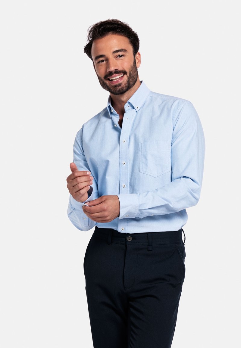 Lichtblauw button-up shirt met een zak; katoenmix stof; lange mouwen; gedragen met donkere broeken; model past de manchet aan.