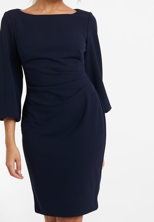 Robe bleu marine avec un décolleté carré, des manches évasées trois-quarts et une silhouette ajustée. Confectionnée dans un tissu lisse avec des détails de drapé subtils.