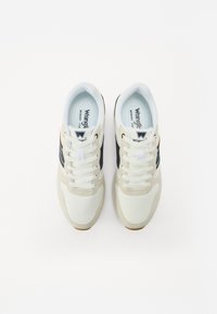 Fehér bőr- és velúr sneaker, fekete oldalsávval, fehér fűzőkkel és texturált gumitalppal. A modell neve belül látható.