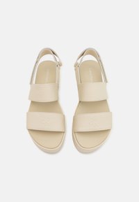 Light beige sandals with two wide fabric straps and a textured sole. Features a subtle embossed logo on the toe strap.