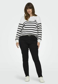 Sudadera a rayas en blanco y negro con cuello redondo y mangas largas, combinada con jeans slim-fit negros y zapatillas blancas.