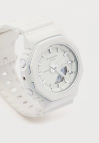 Balta G-Shock laikrodis su aštuonkampiu korpusu, skaitmeniniu ir analoginiu ekranu, sidabro akcentais ir tekstūruotu guminėmis apyrankėmis. Atsparus vandeniui.