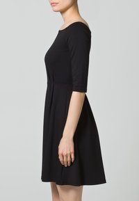 Czarna, bawełniana sukienka z rękawami o długości trzech ćwierć, dopasowana w bodice, rozszerzająca się w talii, z okrągłym dekoltem i gładką teksturą.