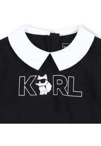 Black top with a white collar featuring the text "KARL" and a cartoon cat wearing sunglasses. Smooth fabric with a fitted design.