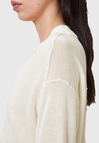 Leichter Strickpullover auscremiger Wolle mit durchsichtigen, strukturierten Stoff, rundem Ausschnitt und dezenten Nähten an den Ärmeln.