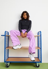 Black long-sleeve top with white accents, purple wide-leg trousers, and white sneakers with black details on a wooden shelf with blue metal frame.