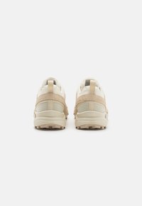 Beige and cream sneakers with textured mesh and smooth panels. Features a cushioned sole and padded collar, designed for comfort and support.