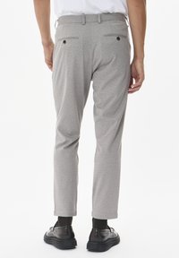 Pantalones grises de textura con un ajuste a medida, bolsillos traseros con botones y zapatos negros contrastantes. Una cintura elástica completa el look.
