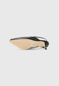Zwarte gepatenteerde leren slingback schoen met spitse neus, dunne hak en gestructureerde beige buitenzool. Heeft een decoratieve accent nabij de hak.