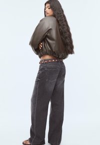 Braune Lederbomberjacke, hoch geschnittene graue weite Jeans mit einem braunen Gürtel mit goldenen Nieten und einem strukturierten Stoff.