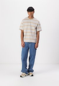 Short-sleeve beige t-shirt with horizontal white and dark brown stripes, paired with blue loose-fit jeans and beige sneakers.