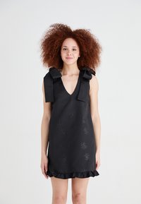 Black dress with a V-neck, featuring textured fabric, floral patterns, and large bows on the shoulders. It has a ruffled hemline.