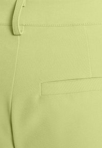 Světle zelené kalhoty s hladkým povrchem, které mají boční kapsu a poutka na opasek, prošívané detaily a střih přizpůsobený postavě.