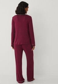 Bordó dvoudílná pyžamová sada obsahující top s dlouhým rukávem a bílým lemovaným límcem a odpovídající široké kalhoty, vyrobená z měkké tkaniny.