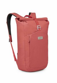 Mochila Osprey en color coral, fabricada con un material duradero. Presenta un cierre tipo rollo, correas ajustables y un bolsillo frontal para almacenamiento.