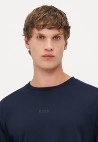 T-shirt azul-marinho feito de um tecido suave, com um clássico decote redondo e um discreto logótipo "BOSS" no peito. Design simples e elegante.