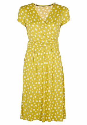 Żółta sukienka kopertowa z krótkimi rękawami, ozdobiona białymi okrągłymi kropkami, z dekoltem w serek i zwiewną, marszczoną spódnicą. Miękka faktura tkaniny.