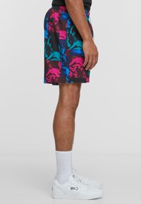 Colorful swim shorts with a vibrant abstract pattern in pink, blue, and black. Made of lightweight fabric, featuring an elastic waistband.