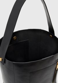Czarna skórzana torba typu bucket o gładkim wykończeniu, z złotymi akcentami metalowymi i przestronnym wnętrzem. Posiada szeroki, płaski pasek na ramię.