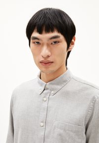 Lichtgrijze overhemde met kraag, van textuurstof en met een borstzak. Voorzien van witte knopen langs de voorpas.