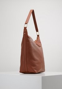 Ruskea nahkalaukku, jossa on pehmeä ja teksturoitu pinta. Varustettu yhdellä olkahihnalla ja kultasävyisellä vetoketjulla ylhäällä.