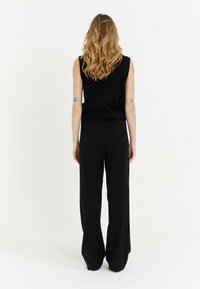 Zwart mouwloos topje en wijde zwarte broek. De stof lijkt zacht met een geribbeld patroon. De silhouet is ontspannen en comfortabel.