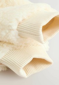Krämfärgad sweatshirt med en mjuk, fluffig textur och ribbad stickad ärmar. Designen inkluderar en plyschkropp och kontrasterande elastiska kanter.