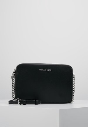 Sort rektangulær crossbody-taske med sølv kæderem og "Michael Kors" logo centreret foran, udstillet på en hvid piedestal.