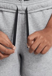 Grijze joggingbroek met een tailleband met trekkoord. De koorden zijn zwart en de stof heeft een zachte, gestructureerde uitstraling. Close-up van handen die de koorden verstellen.