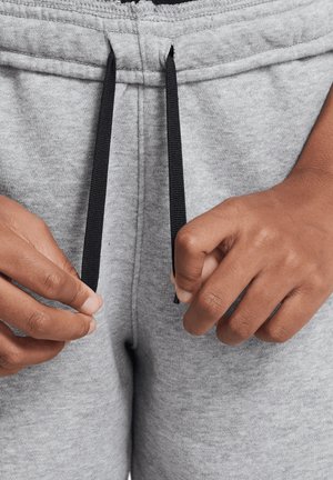 Pantalon de survêtement gris avec taille à cordon de serrage. Les cordons sont noirs et le tissu a une apparence douce et texturée. Gros plan sur des mains ajustant les cordons.