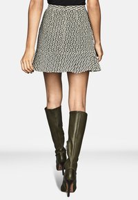 Černo-bílá vzorovaná sukně do áčka s přiléhavým pasem, v kombinaci s olivově zelenými koženými holinkami sahajícími ke kolenům a na vysokém podpatku.