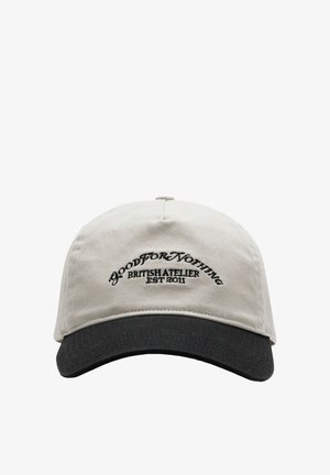 Beige fabric cap with a black brim; features curved shape and embroidered text “GOOD FOR NOTHING BRITISH ATELIER EST 2011” on the front.