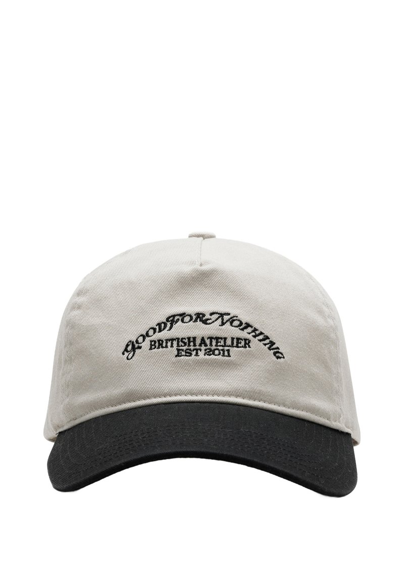 Cappello di stoffa beige con visiera nera; presenta una forma curva e testo ricamato "GOOD FOR NOTHING BRITISH ATELIER EST 2011" sul davanti.