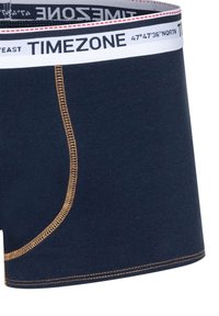 Navy cotton boxer shorts with a white waistband featuring “TIMEZONE.” Accent stitching in gold along the seams. Smooth texture.