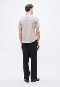 Szara koszulka polo z krótkim rękawem i prostym dołem, zestawiona z czarnymi spodniami i czarnymi butami. Materiał wydaje się gładki z subtelną fakturą.