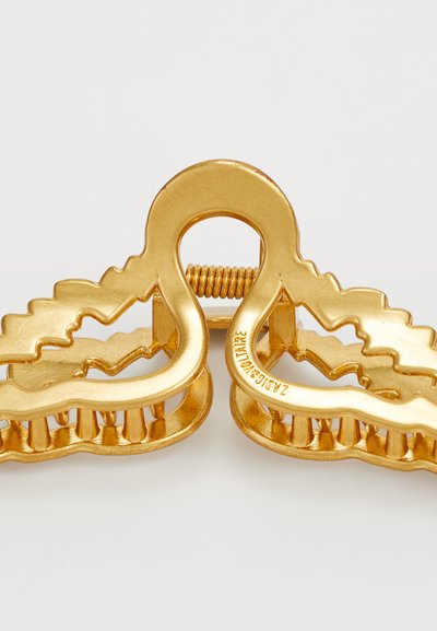 Čelična zlatna kvačica za kosu s valovitim dizajnom, teksturiranim zubima za bolji zahvat i središnjim vijakom za zatvaranje. Glatka metalik završna obrada.