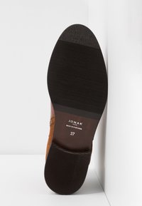 Sål af en brun lædersko med sort gummihæl og tågreb, mærket "JONAK Paris Made in Portugal" og størrelse 37.