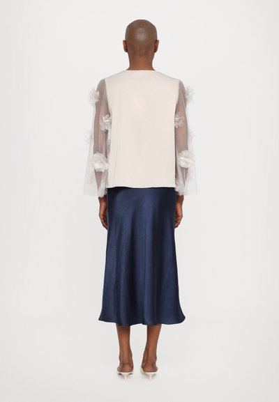 Light cream top with sheer sleeves adorned with white floral accents, paired with a flowing navy satin skirt. Smooth texture and elegant silhouette.